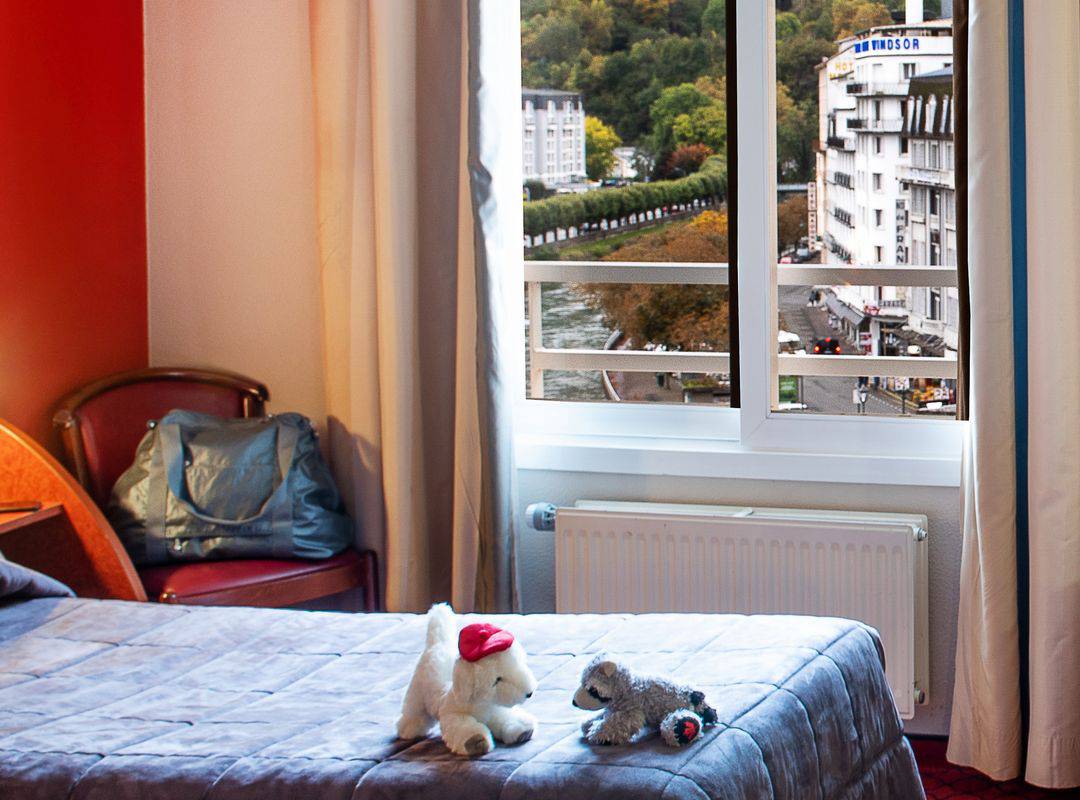 Room with two single beds with stuffed animals on the bed and a view of the houses and nature, accommodation occitanie – Hotel la Solitude